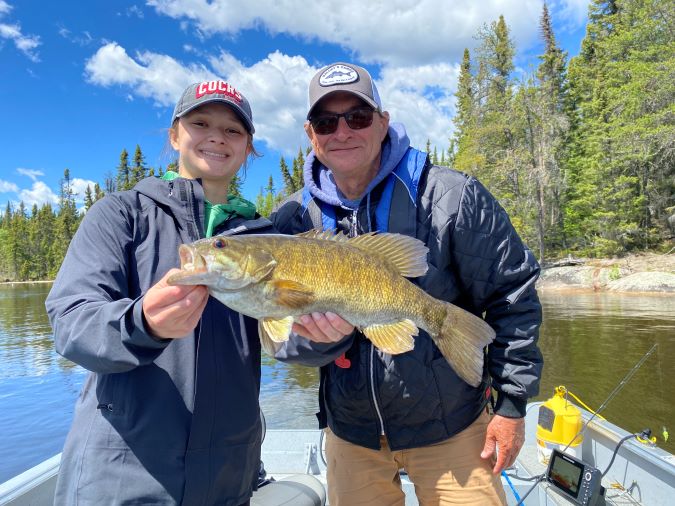 Youngster fisherman and guide with trophy smallmouth bass-sunny day, bright colors and blue sky.