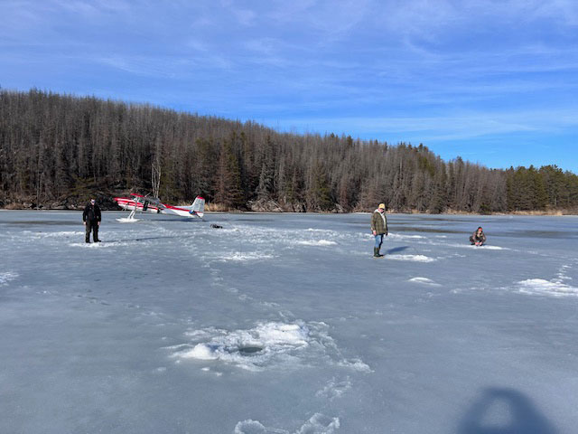 Group ice fishing with a plane on skis in the background