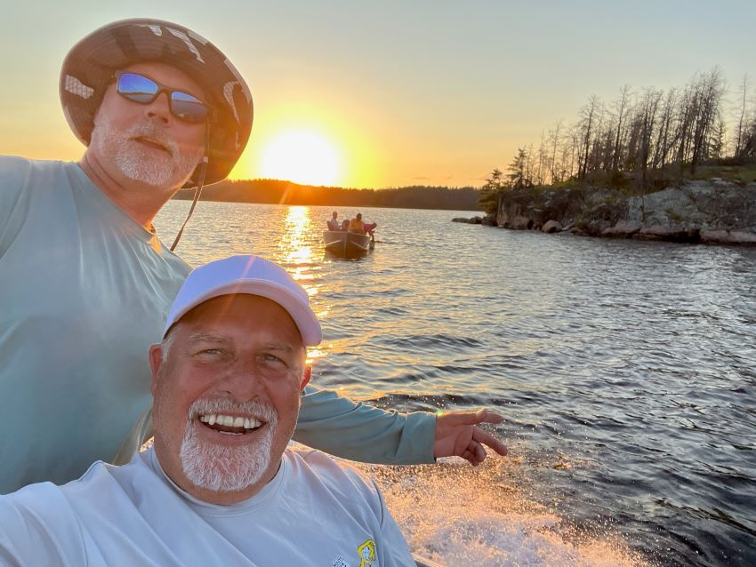 Friends in fishing boat with sunset behind them at Halley's Camps Trapline Lake Outpost.