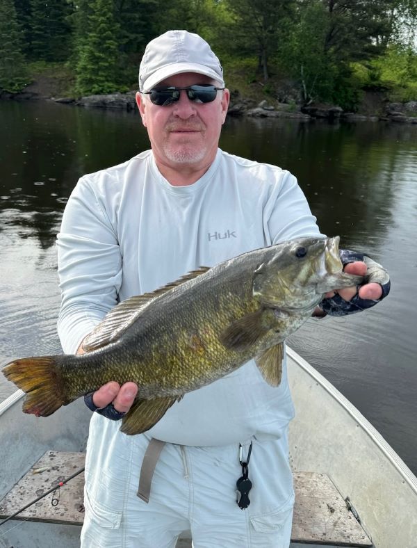 Man holding big bass with calm waters behind him as he fishes from a boat at Rex Lake Outpost.