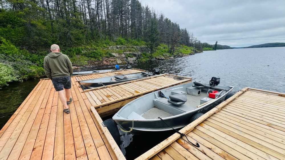 Man walking down the new docks at Rex Lake Outpost with the 3 boats parked at the dock.