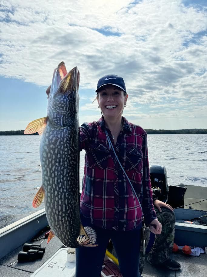 Lade holding up trophy northern pike with the English River in the background fishing out of a Halley's Camps boat.