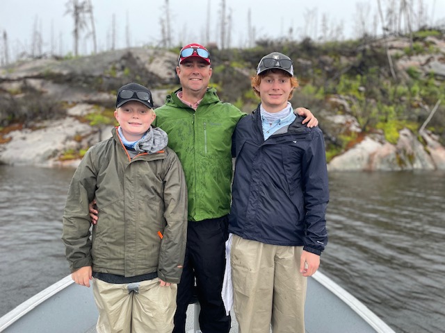 Father and 2 sons standing smiling at the front of the boat.