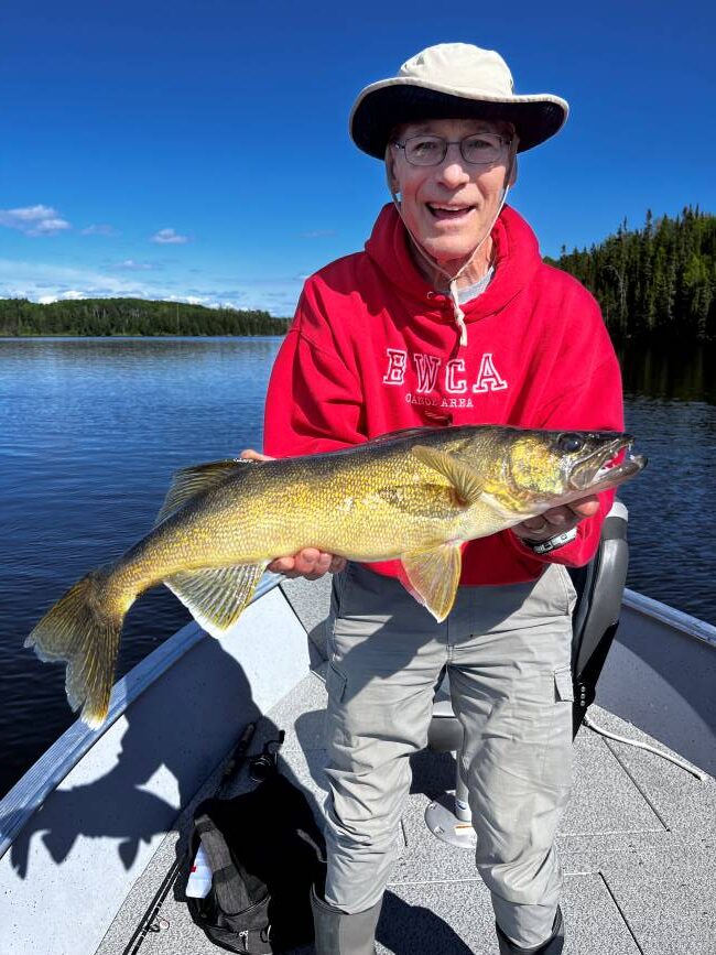 Doug holding up his walleye with the beautiful Canadian scenery behind him.