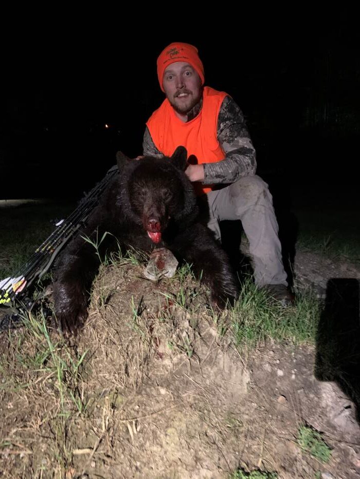 Hunte wearing orange holding up his black bear head and posing after his successful bear hunt at Halley's Camps!