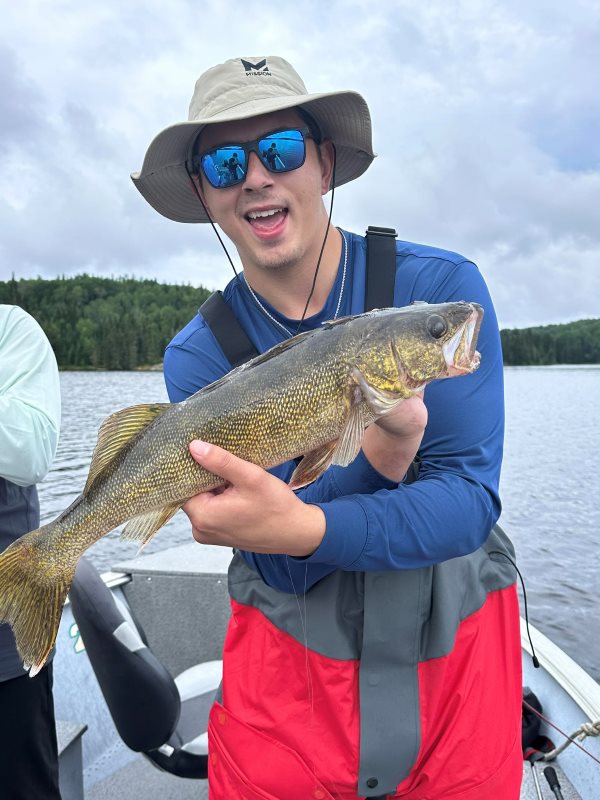 Man holding a walleye in a boat on the English River at Halley's Camps!