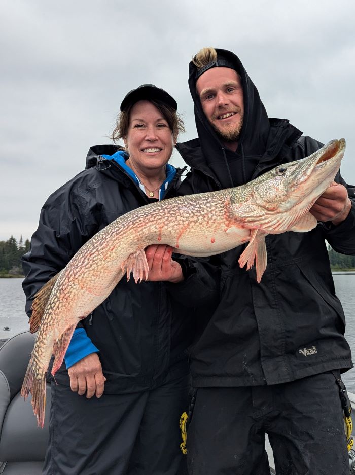 Woman standing with her guide at Halley's Camps in a boat and holding trophy northern pike!