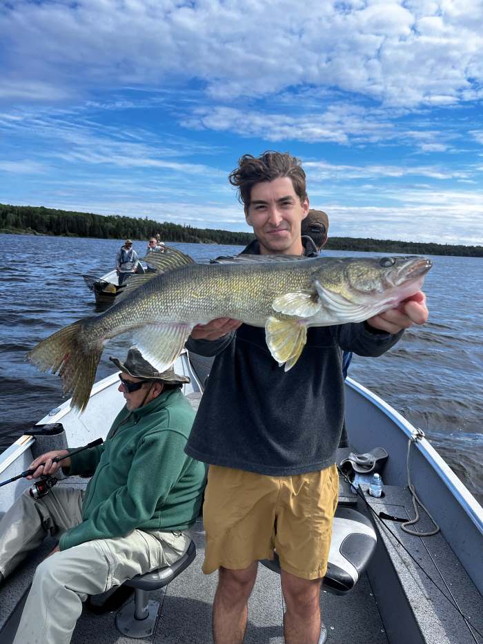 Fisherman with his hat off holding large walleye with his grandpa!