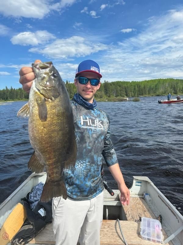 A man holding up a trophy smallmouth bass in a boat.