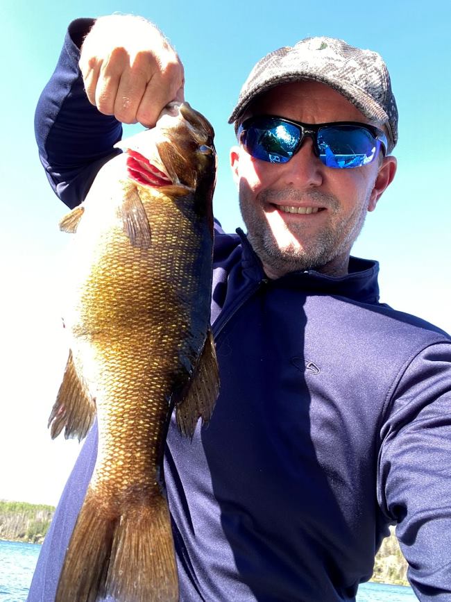 Fisherman posing with his smallmouth bass in a fishing boat at Halley's Camps!