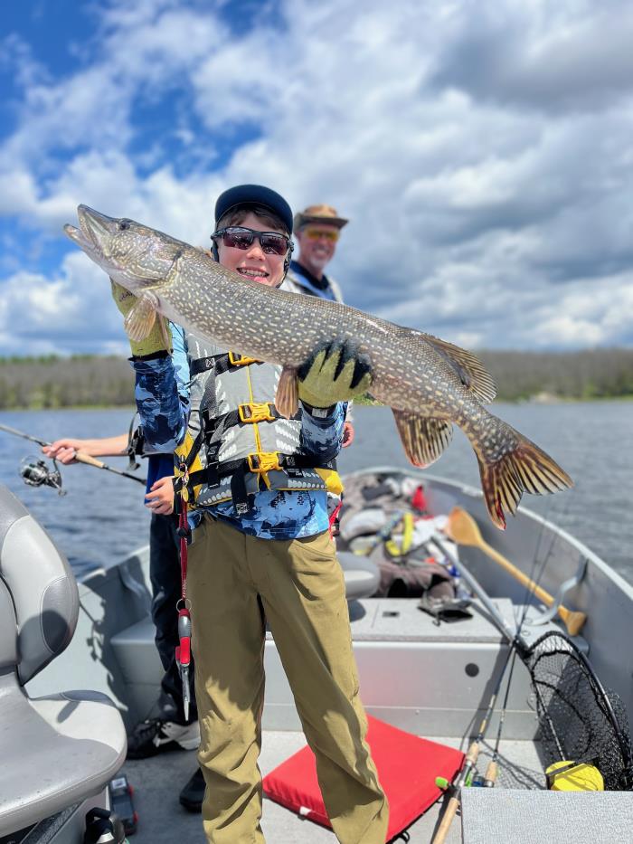 Child holding up a northern pike fish in the front of a boat