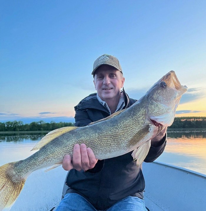 Tom holding a big walleye at the front of a boat.