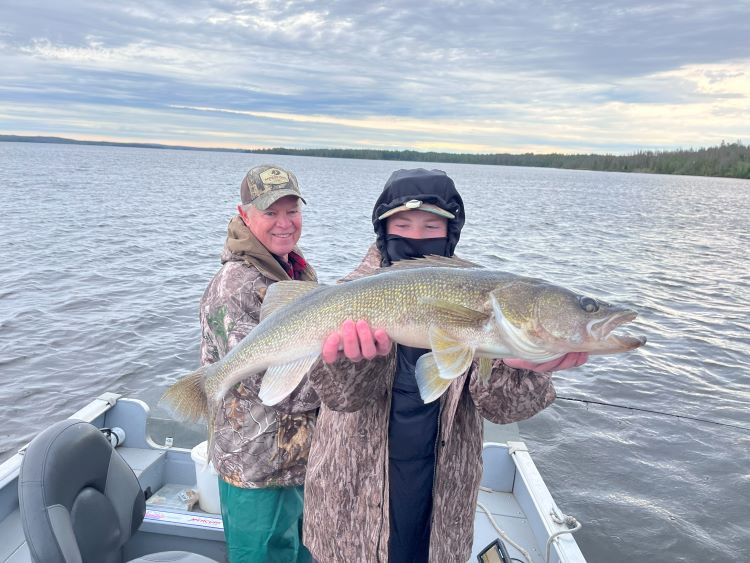 Grandpa and grandson fishing with grandson holding big walleye.