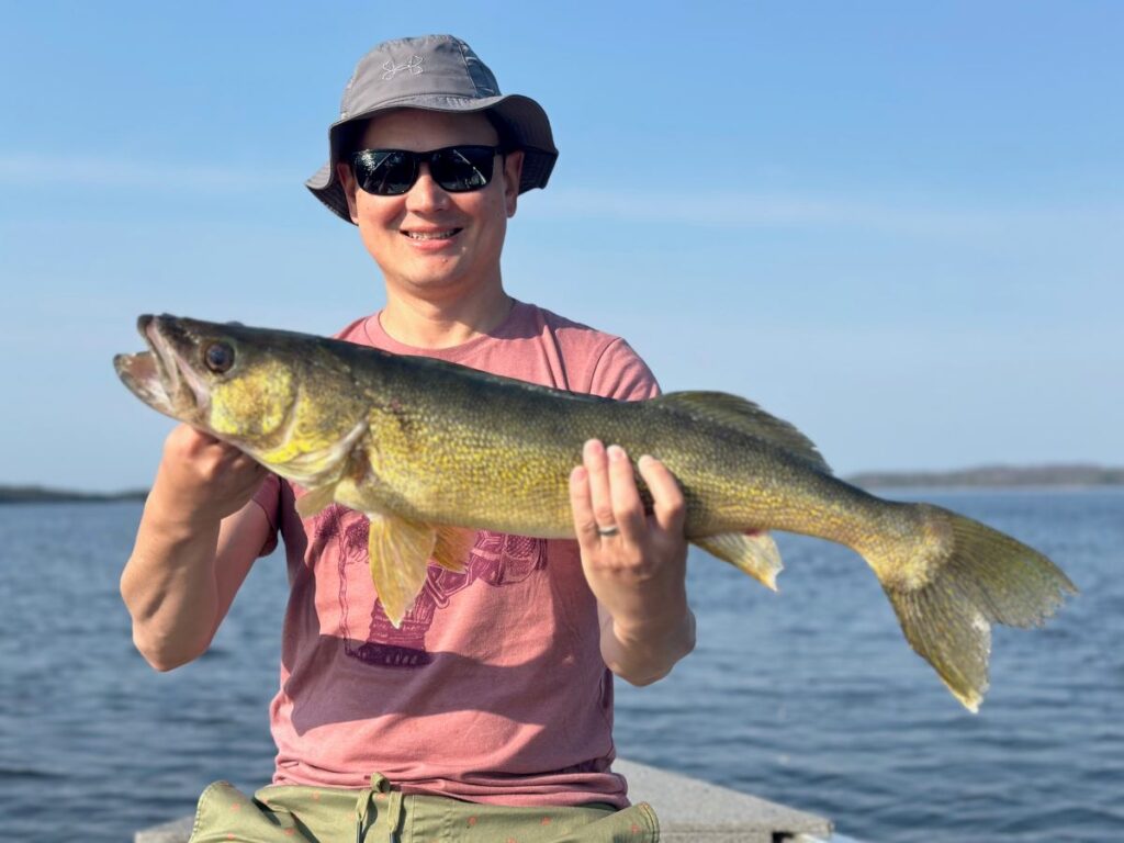 Fishman holding a walleye in the front a of a Halley's Camps Fishing boat.