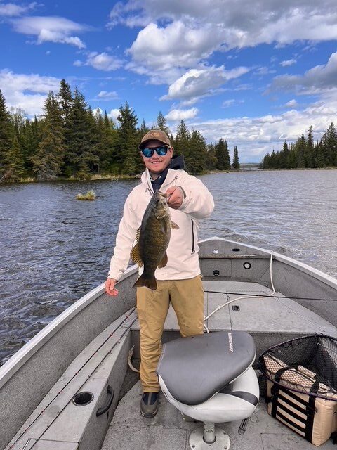 Young man holding bass out of a boat on a sunny day at Halley's Camps.