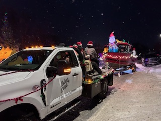 Heavy duty Halley's Camps truck with people sitting on back. Truck is pulling a red boat with Santa in the front of the boat!